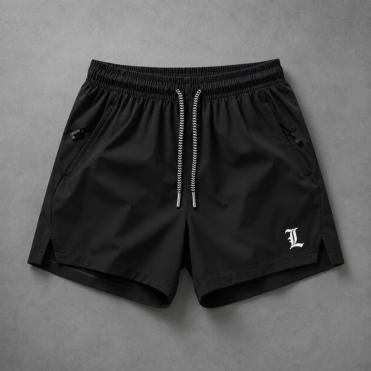 Black athletic shorts with a white drawstring and a white Gothic-style 'L' logo on the lower left leg, laid flat on a textured gray background.